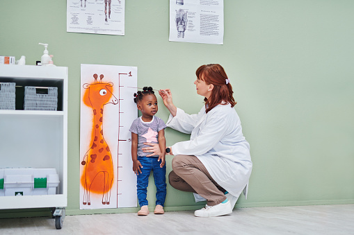 Foto de un médico que mide la altura de una adorable niña durante una consulta photo