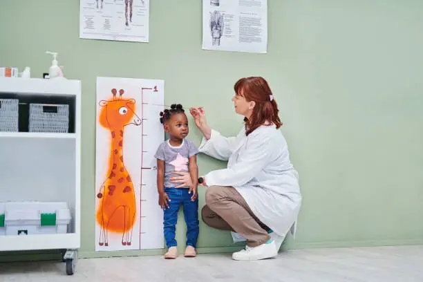 Photo of Shot of a doctor measuring an adorable little girl’s height during a consultation