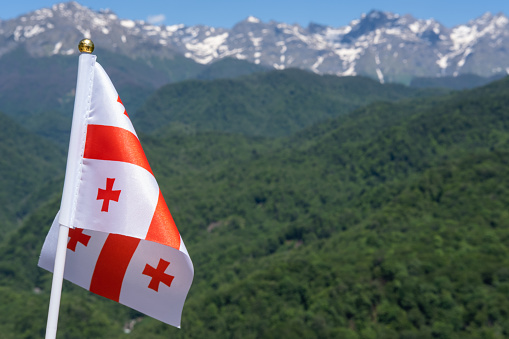 Georgia Flag Waving on Background of Mountains and Blue Sky. Tourism to Learn the Traditions of Different Peoples