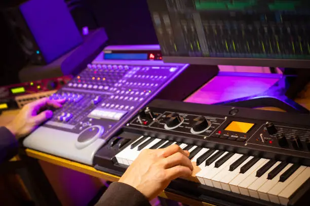 Photo of music producer, arranger, DJ hands remixing music on synthesizer keyboard, control surface and computer in home recording studio