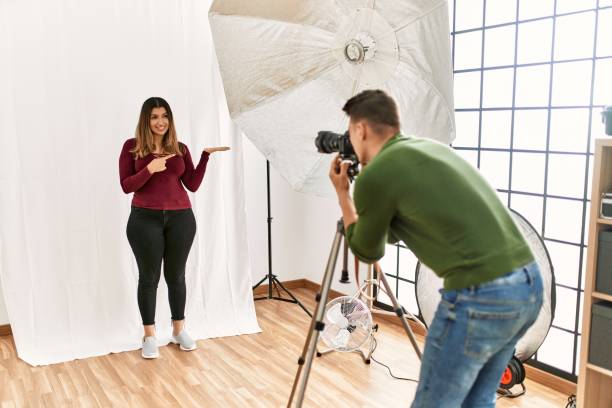 istock Young woman at photography studio amazed and smiling to the camera while presenting with hand and pointing with finger. 1327844037