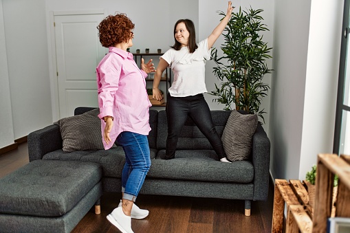 Mature mother and down syndrome daughter at home dancing on the sofa