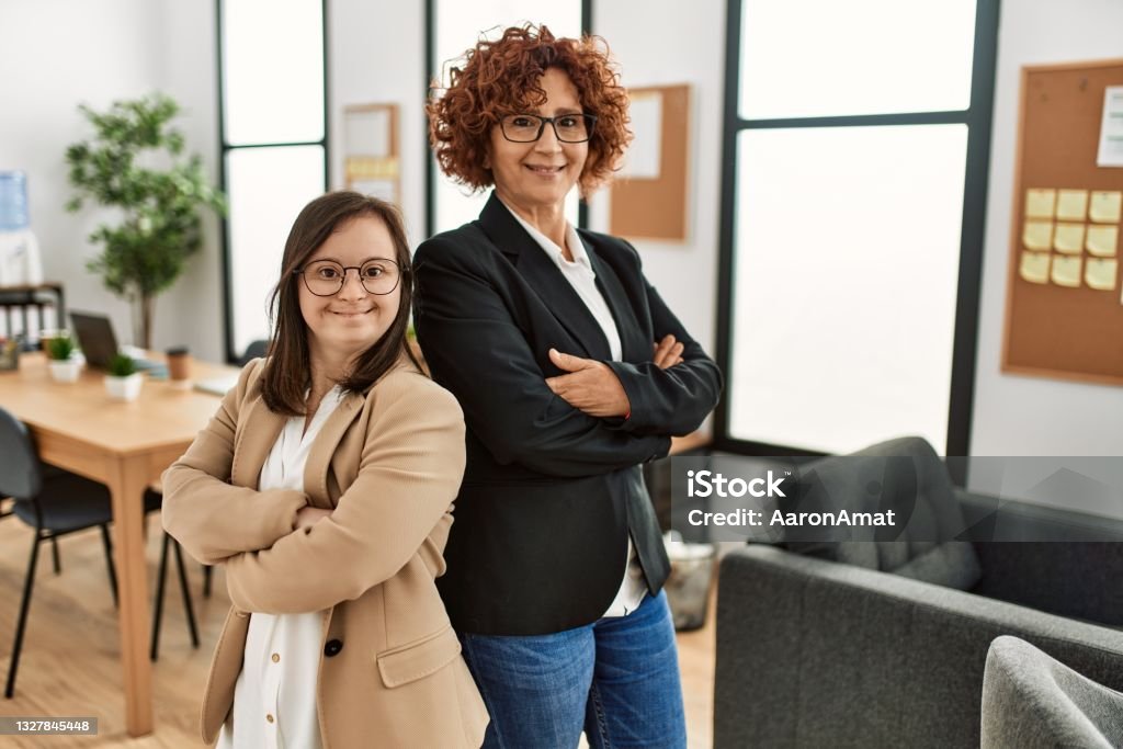 Group of two women working at the office. Mature woman and down syndrome girl working at inclusive teamwork. Down Syndrome Stock Photo