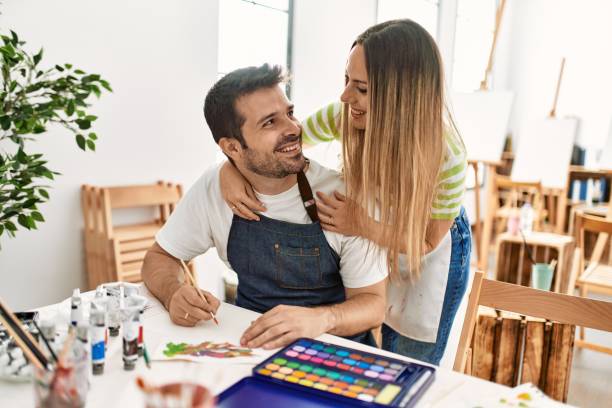 istock Two students smiling happy painting sitting on the table at art school. 1327846103