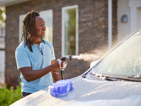 A young couple washing a car in a driveway on a summer evening.