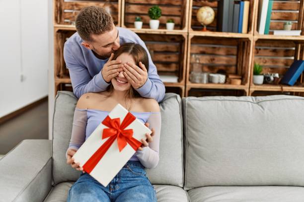 istock Young man surprising his girlfriend with birthday gift at home. 1327846965