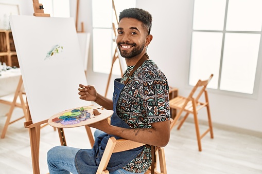 Young african american artist man smiling happy painting at art studio.