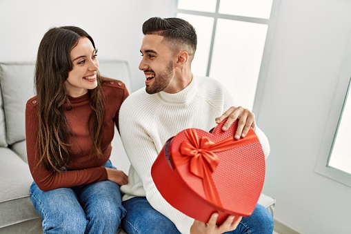 Young hispanic couple smiling happy surprising with valentine gift at home.