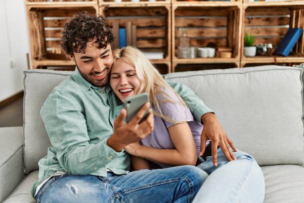 istock Young couple using smartphone sitting on the sofa at home. 1327847877