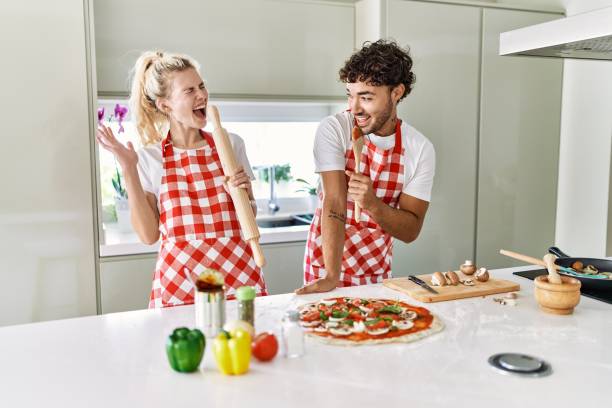 istock Young couple smiling happy and singing using kneader and spoon as a microphone at kitchen. 1327847961