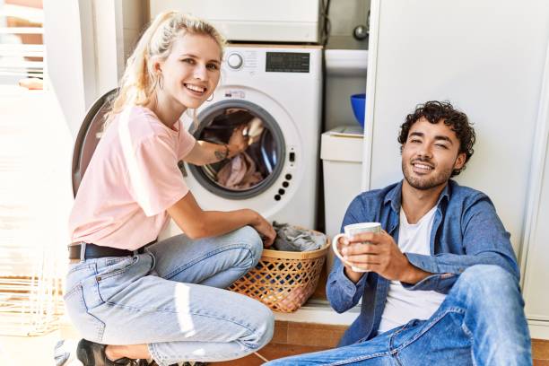 młoda para uśmiechająca się szczęśliwie pijąc kawę podczas prania w domu. - family with one child domestic life caucasian love zdjęcia i obrazy z banku zdjęć
