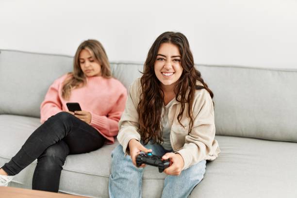 istock Girl playing video game and her girlfriend boring using smartphone at home. 1327848610