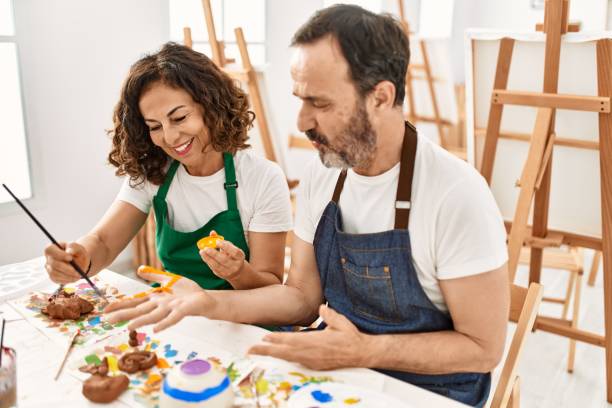 istock Two middle age student smiling happy painting hands at art studio. 1327848853