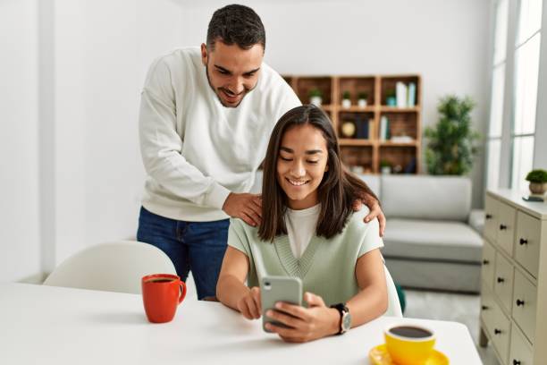 自宅でスマートフォンを使用して幸せ笑顔若いラテンカップル。 - family room ストックフォトと画像