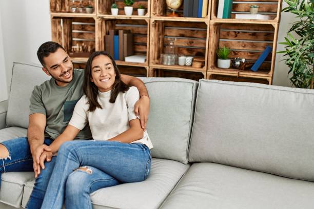 istock Young latin couple sitting on the sofa hugging at home. 1327850449