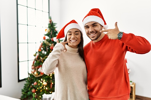 Young hispanic couple standing by christmas tree smiling cheerful showing and pointing with fingers teeth and mouth. dental health concept.