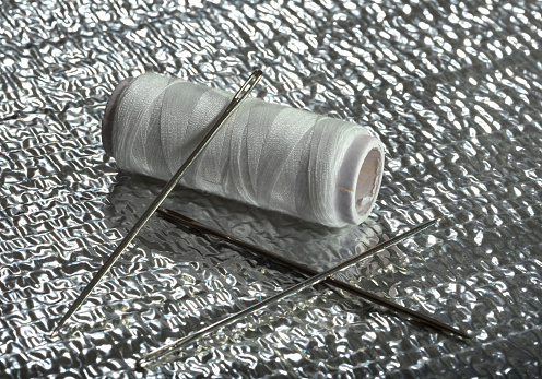 White thread and needle on a silver background.