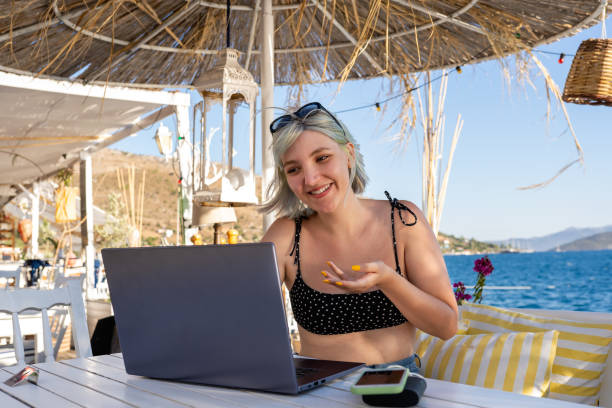 istock Young woman having a video call on the beach 1327870378