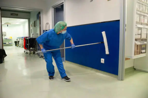 Woman from the cleaning service of a hospital cleaning the walls of the pre-operating room with a special brush. Sanitary concept