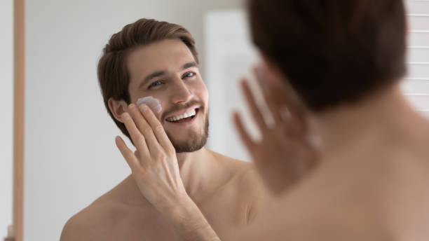 istock Happy handsome metrosexual guy applying sunscreen on face at mirror 1327874239