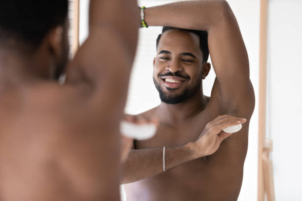 Calm handsome young well built man using deodorant, applying antiperspirant