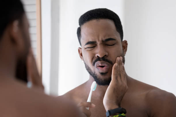 Stressed upset mixed raced Black man feeling pain and discomfort Stressed upset mixed raced Black man feeling pain and discomfort while brushing teeth in bathroom, holding toothbrush, touching cheek with painful grimace. Toothache, dental problem concept toothache stock pictures, royalty-free photos & images