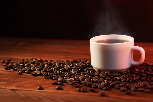 Warm cup of coffee and coffee beans on dark background. Coffee cup and coffee beans on wooden table.