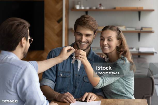 Happy Young Male Real Estate Agent Giving Keys To Couple Stock Photo - Download Image Now