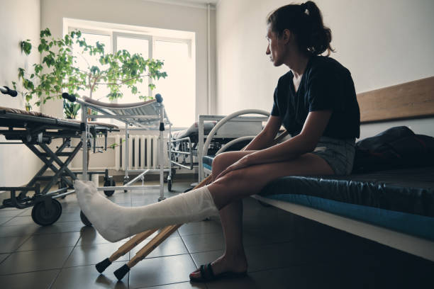A woman with a broken leg sits on a hospital couch and looks out the window. Leg injury. Loss of mobility. Rehabilitation after a fracture A woman with a broken leg sits on a hospital couch and looks out the window. Leg injury. Loss of mobility. Rehabilitation after a fracture. broken leg stock pictures, royalty-free photos & images