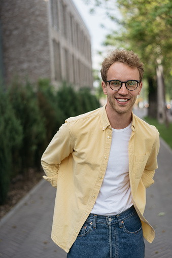 Portrait of young smiling teenager wearing casual yellow shirt, stylish eyeglasses walking on the street. Confident university student looking at camera, education concept