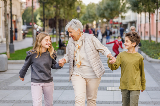 An Older Woman is Enjoying the Time with her Grandchildren While Holding Hands and Walking Through the City Streets.