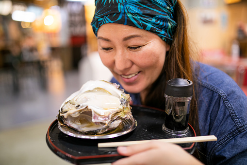 A Japanese woman looking with a smile at a huge fresh Oyster on a plate.