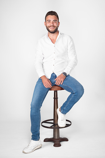 Young man in a white shirt and blue jeans poses against a white background.