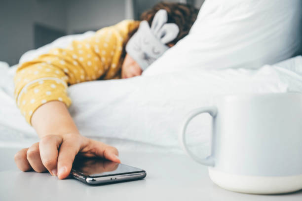 Woman in sleeping mask being woken by mobile phone In bedroom. Woman in sleeping mask being woken by mobile phone In bedroom. alarm clock snooze stock pictures, royalty-free photos & images