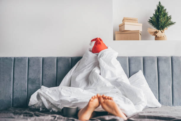 svegliati la mattina dopo le vacanze di festa. donna in cappello di babbo natale sotto coperta a letto. - holiday emotional stress christmas santa claus foto e immagini stock