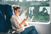 Young woman traveling by train and using phone.
