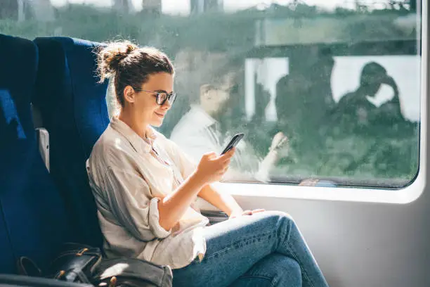 Photo of Young woman traveling by train and using phone.