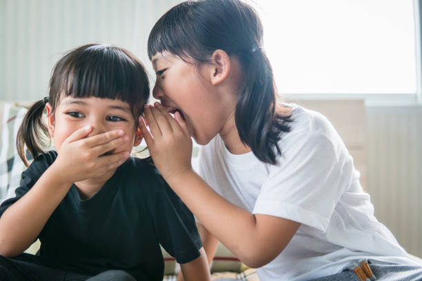 istock happy little Asian siblings sharing secrets 1327903329