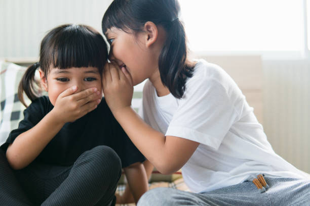 istock happy little Asian siblings sharing secrets 1327905826