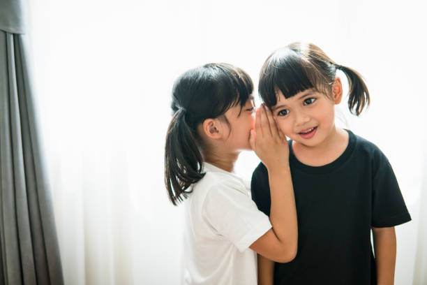 istock happy little Asian siblings sharing secrets 1327905830