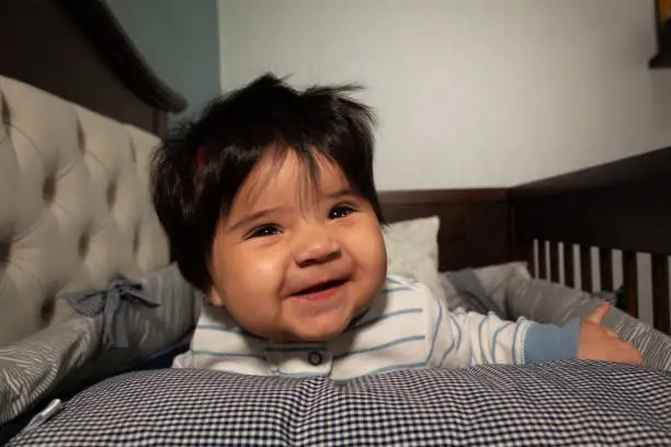 portrait of a 5 month old hispanic baby with long hair and very smiling and happy face