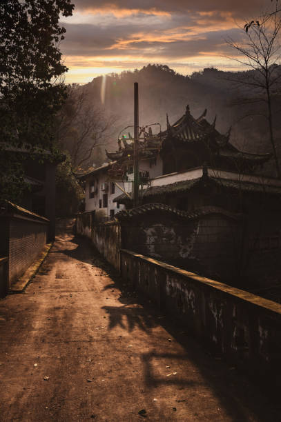 Old Chinese building, moody dark golden hour view en camino a la montaña qingcheng, sichuan, china. impresionante puesta de sol de la hora de oro sobre las montañas y la antigua casa de construcción de estilo chino asiático cerca del camino de la carretera. arquitectura tradicional y lanzas en el bord
