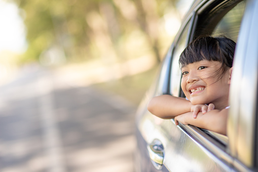 Cute asian little child girl having fun to travel by car and looking out from ar window in cthe countryside
