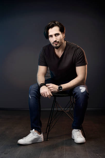 istock A handsome young man sitting at dark background while looking at camera. 1327914851