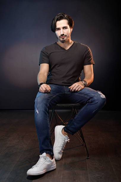 istock A handsome young man sitting at dark background while looking at camera. 1327915666