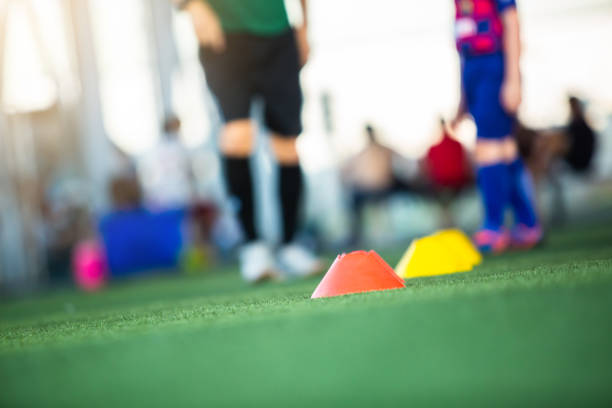 istock Selective focus to cone marker with blurry soccer team is on green artificial turf. 1327918670