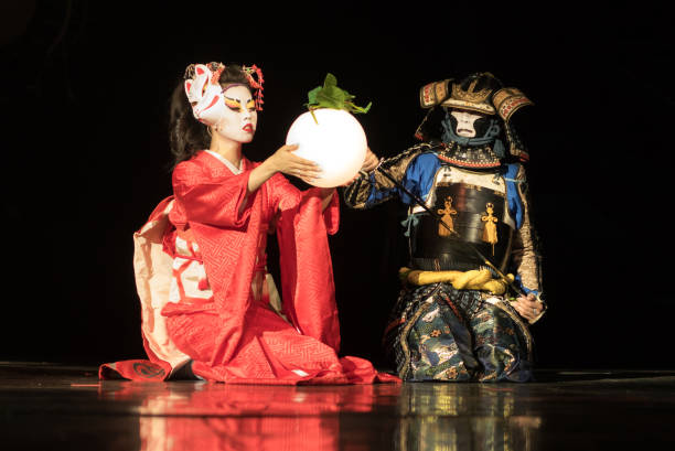 geisha japonesa en kimono tradicional y máscara de zorro sosteniendo la lámpara de la esfera y samurai guerrero en armadura están sentados de rodillas en la oscuridad. actuación tradicional japonesa. - kabuki fotografías e imágenes de stock