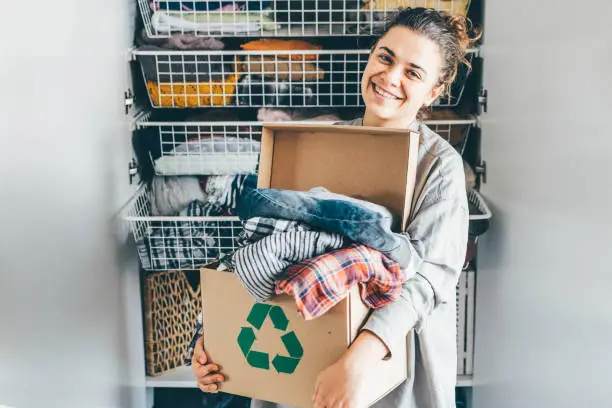 Photo of Recycle clothes concept. Young woman with recycling box full clothes.