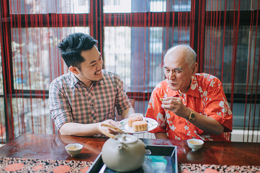 Chinese son sharing mooncake to his father during traditional mid-autumn festival at home during afternoon tea gathering