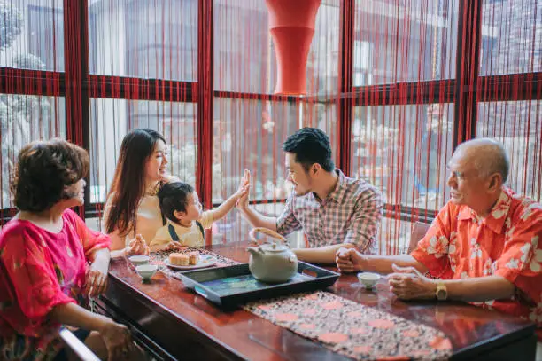 Chinese father high five with son during enjoying traditional mid-autumn mooncake and chinese tea at home during afternoon tea gathering